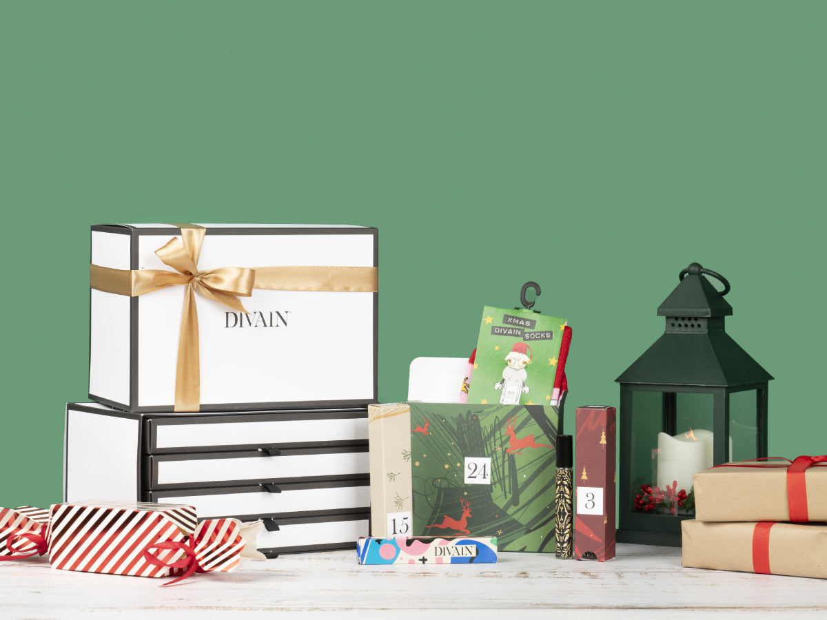 Beauty-Adventskalender der Marke Divain Parfums mit einer Auswahl an Parfums, Kosmetik und Accessoires auf einem weihnachtlichen Hintergrund.